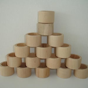 May include: A stack of 15 natural wood napkin rings arranged in a pyramid shape. The rings are all the same size and are made of unfinished wood.