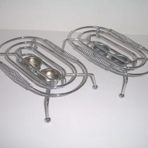 May include: Two silver metal candle holders with three candle cups each. The holders have a spring-like design and stand on four legs.