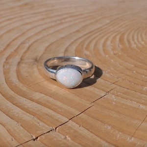May include: A silver ring with a white opal gemstone. The ring is on a wooden surface.