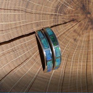 May include: Two silver bands with a row of blue and green opal stones set in each band.