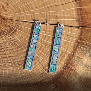 May include: A pair of silver earrings with a long, rectangular design. Each earring is filled with small, iridescent opal pieces.