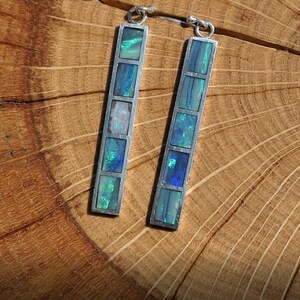 May include: A pair of silver dangle earrings with a rectangular design. Each earring features five iridescent opal stones set in silver.