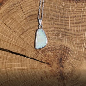 May include: A silver chain necklace with a pendant featuring a white opal stone set in a silver frame.