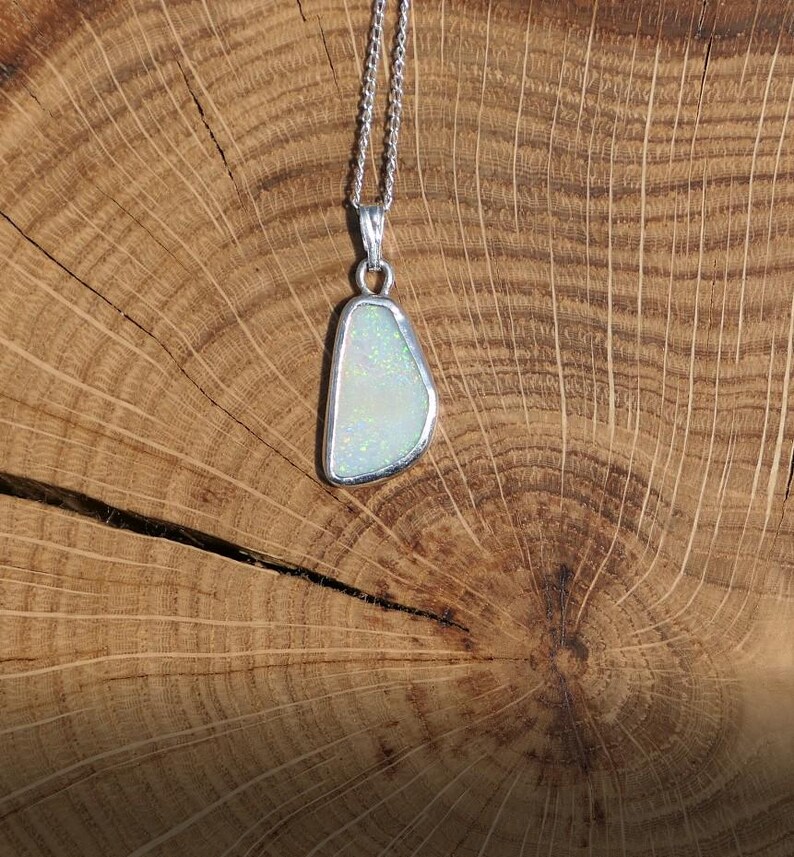 May include: A silver chain necklace with a pendant featuring a white opal stone set in a silver frame.