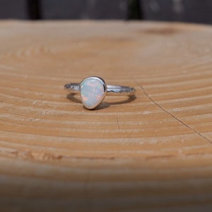 May include: A silver ring with a white opal gemstone. The ring is on a wooden surface.