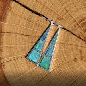 May include: A pair of silver earrings with a triangular shape. Each earring is made up of multiple pieces of iridescent green and blue opal.