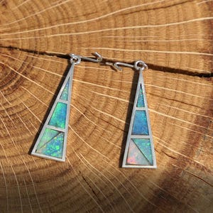 May include: A pair of silver earrings with a geometric design featuring iridescent opal stones. The earrings are triangular in shape and have a silver hook fastening.