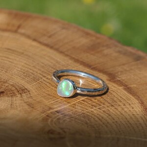May include: A silver ring featuring an opal gemstone. The opal is pear-shaped and displays a milky white base with green and yellow flashes. The ring band has a hammered texture.