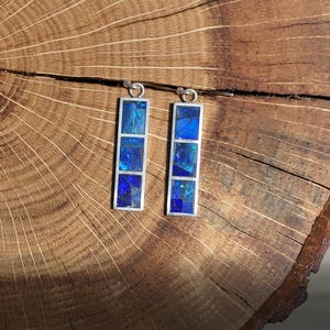 May include: A pair of silver earrings with blue opal stone accents. Each earring features four square-shaped stones set in a silver frame.