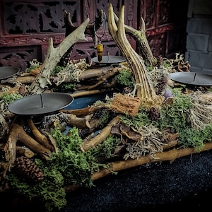 Può includere: Una ghirlanda natalizia rustica in legno con quattro portacandele, decorata con corna, muschio, pigne e altri elementi naturali.