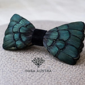 Puede incluir: Pajarita artesanal de plumas verde oscuro con centro de terciopelo negro. Este accesorio formal es perfecto para ocasiones especiales. El nombre de la marca "DABA AUSTRA" está impreso debajo.