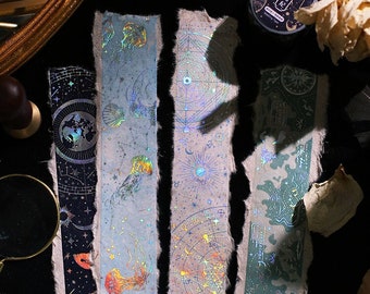 May include: Three decorative washi tapes with iridescent holographic designs. The tapes feature celestial and ocean themes with stars, constellations, jellyfish, and a compass.