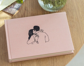 May include: A pink linen-covered journal with a black line drawing of a couple embracing on the front cover.