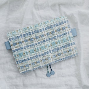 May include: A light blue zippered pouch with a white and blue checkered pattern. The pouch has a light blue zipper pull with two blue tassel charms.