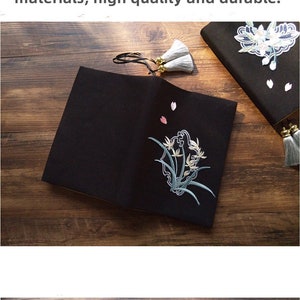 May include: Three different notebook covers with embroidered floral designs. The covers are made of a black fabric, a light gray fabric, and a dark blue fabric. Each cover has a tassel.