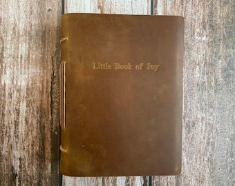 May include: A brown leather-bound journal with the text "Little Book of Joy" embossed on the front cover.