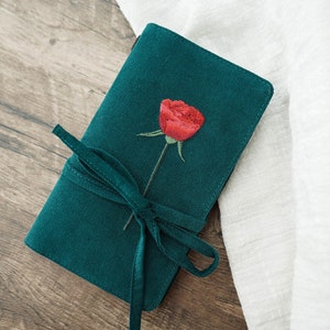 May include: A dark green corduroy notebook with a red embroidered rose and a matching green ribbon tie.