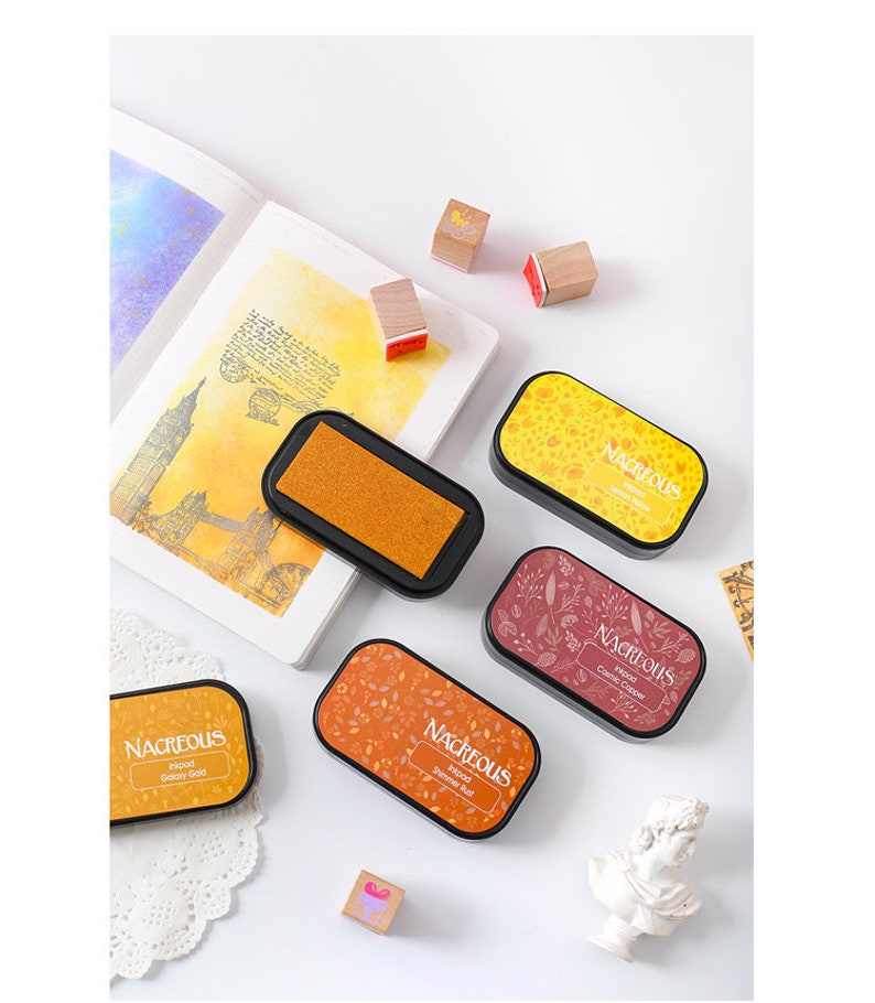 May include: Four ink pads with different colored inks and patterns. The ink pads are labeled "Nacreous" and have the ink color listed below. The ink colors are Galaxy Gold, Summer Rust, Cosmic Copper, and Autumn Leaves.