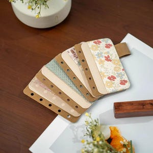 以下が含まれることがあります： さまざまな模様が施された、装飾的なプランナー用インサートのセット。インサートには、花柄、水玉模様、幾何学模様が含まれています。各インサートには、バインディング用の穴が開いた茶色の縁があります。一番上のインサートは、赤、黄、青の花柄です。