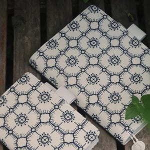 Op de afbeelding: Twee witte stoffen notitieboekhoezen met een blauw geometrisch patroon. De hoezen hebben een witte flap met een witte knop.
