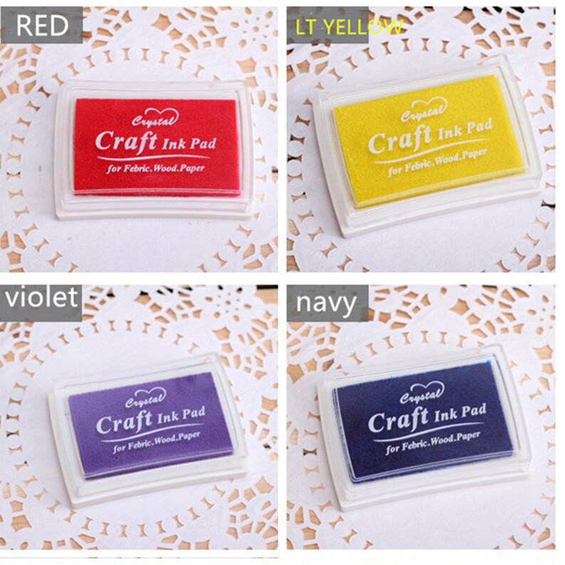 K&ouml;nnte beinhalten: Vier Stempelkissen in verschiedenen Farben: Rot, Gelb, Lila und Blau. Jedes Kissen hat ein wei&szlig;es Plastikgeh&auml;use mit dem Aufdruck "Crystal Craft Ink Pad for Fabric, Wood, Paper".