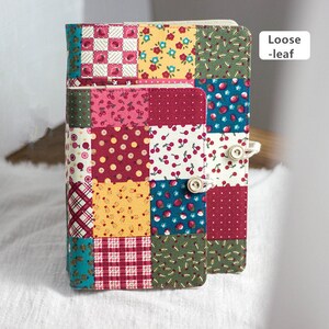K&ouml;nnte beinhalten: Ein Notizbuch mit losen Bl&auml;ttern, das mit einem Patchwork-Stoff in Rot, Gelb, Blau und Gr&uuml;n bezogen ist. Das Notizbuch hat zwei Kn&ouml;pfe an der Seite.