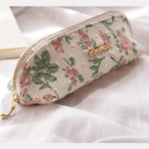 May include: A white zippered pencil case with a floral pattern and gold zipper pull. The case has the word "remarkable" printed in gold on the front.