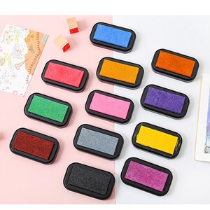 May include: A set of 10 ink pads in various colors, including red, orange, yellow, green, blue, purple, pink, gray, brown, and black. The ink pads are in individual plastic cases with a clear lid.