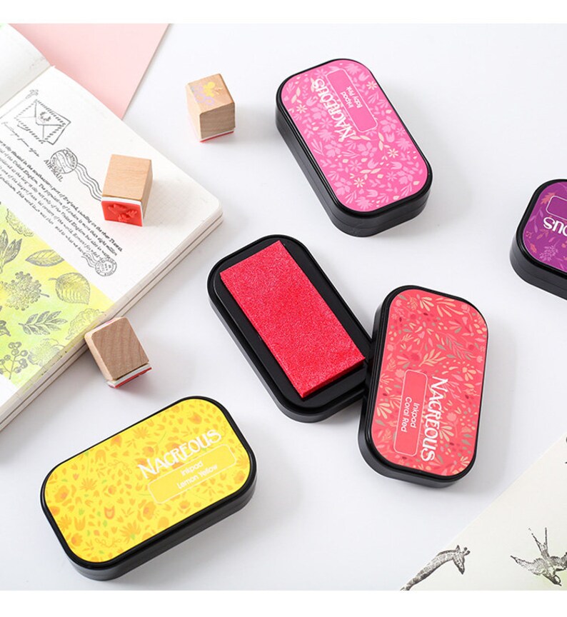 May include: Four ink pads with floral designs and the word "Nacreous" printed on the top. The ink pads are in the colors coral red, lemon yellow, red, and pink.