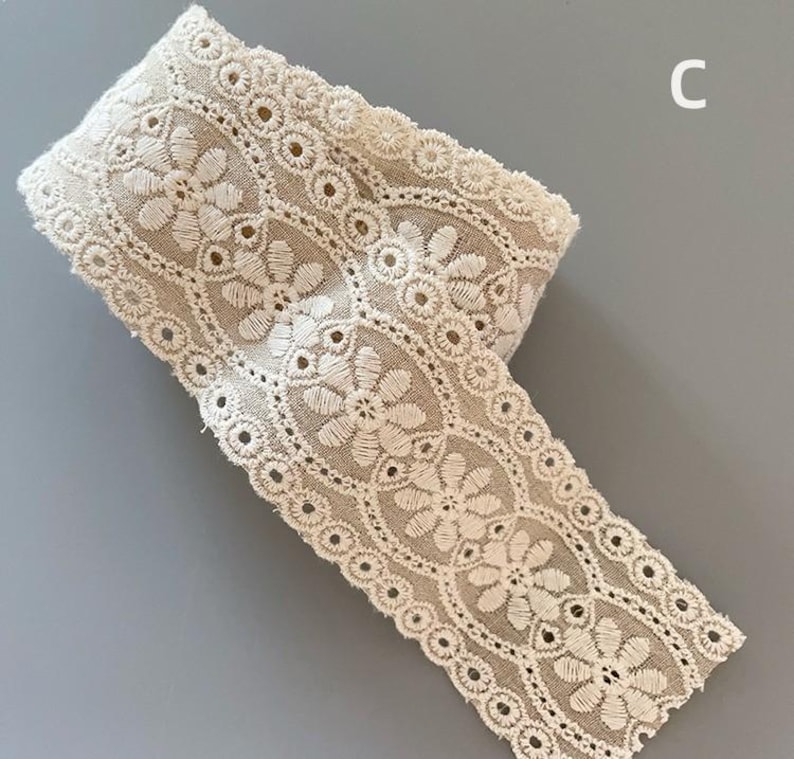 May include: A roll of off-white cotton lace trim with a delicate floral pattern. The lace has a scalloped edge and is perfect for adding a touch of elegance to any project.