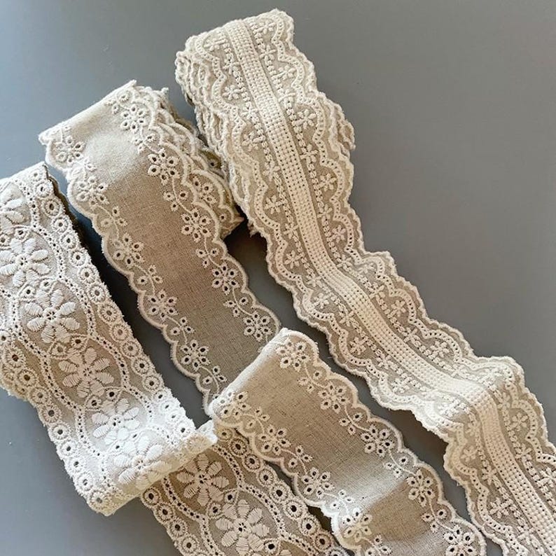 May include: Three different styles of beige lace trim with white embroidery. The lace trim is delicate and intricate, with a variety of floral patterns.