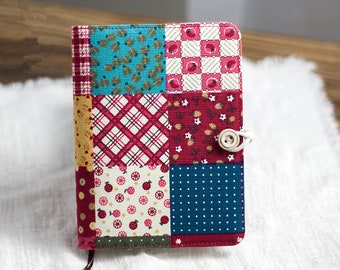 May include: A small, patchwork notebook cover with a variety of colorful patterns, including red, blue, and white. The cover has a button closure and a brown leather strap.