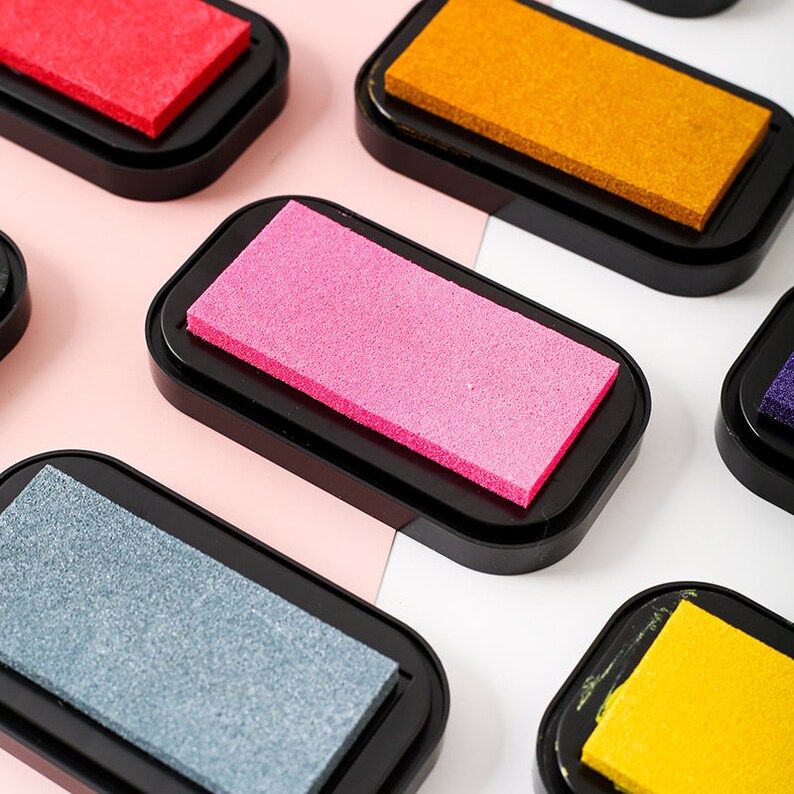 May include: A set of six ink pads in various colors, including red, orange, pink, gray, yellow, and purple. Each pad has a rectangular sponge ink pad in a black plastic case.