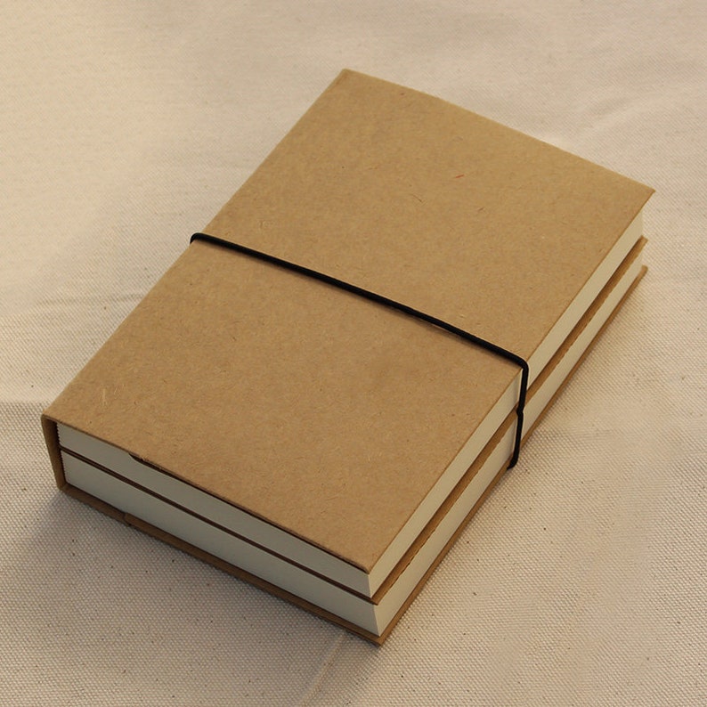 May include: Two brown notebooks bound together with a black elastic band. The notebooks have a simple, minimalist design.