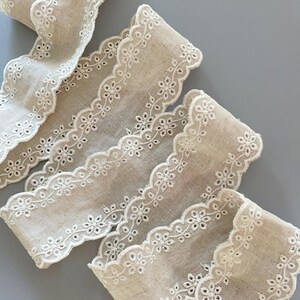 May include: Beige cotton lace trim with a scalloped edge and white embroidered floral details.