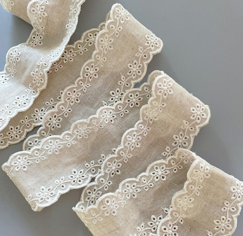 May include: Beige cotton lace trim with a scalloped edge and white embroidered floral details.
