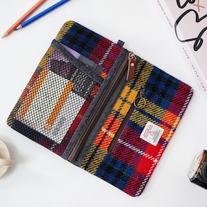 Könnte beinhalten: Mehrfarbig kariertes Federmäppchen mit Reißverschluss und mehreren Fächern. Das Etui hat eine Netztasche, eine kleine Reißverschlusstasche und einen Leder-Reißverschlussanhänger. Der Stoff hat rote, blaue, gelbe und grüne Farbtöne.