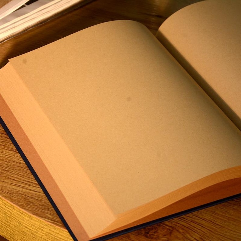 Puede incluir: Un libro abierto en blanco con p&aacute;ginas marrones y una cubierta azul oscuro. El libro est&aacute; abierto sobre una superficie de madera.