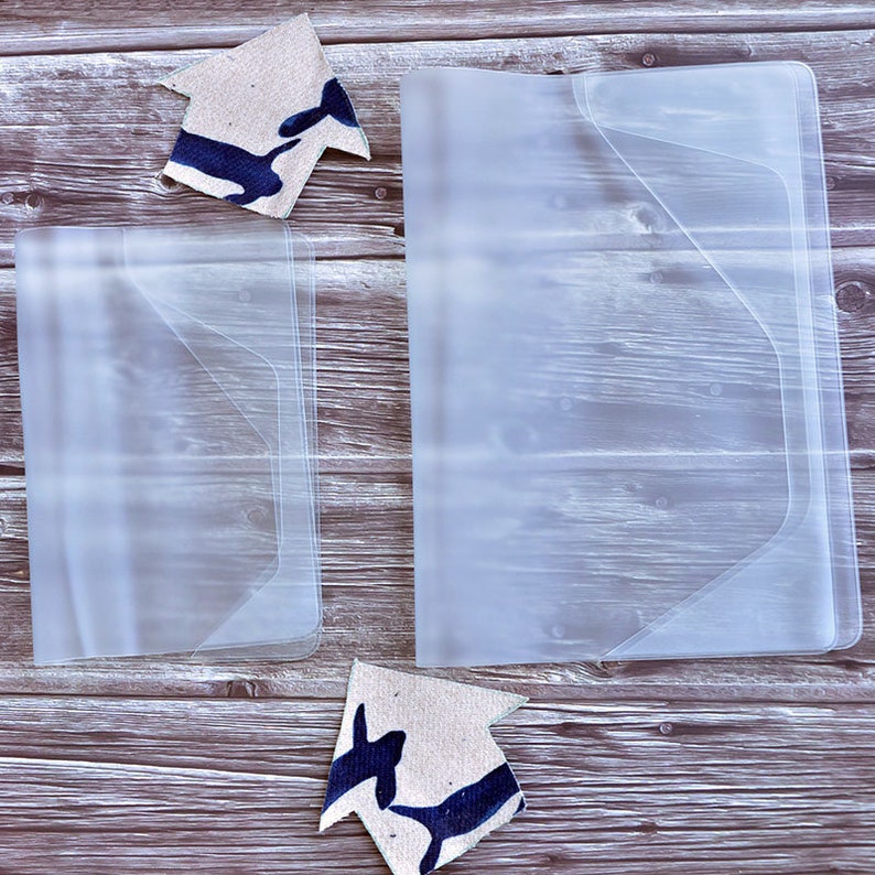 May include: Two clear plastic folders with a flap on the top. The folders are on a wooden surface.