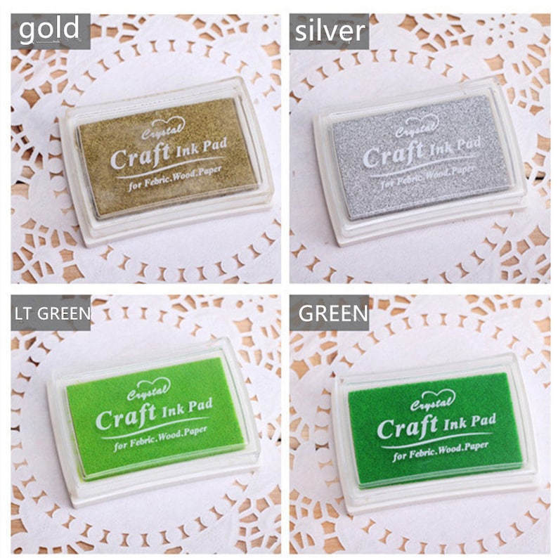 K&ouml;nnte beinhalten: Vier Stempelkissen in verschiedenen Farben: Gold, Silber, Hellgr&uuml;n und Gr&uuml;n. Jedes Kissen hat ein transparentes Kunststoffgeh&auml;use und ein Etikett mit der Aufschrift "Crystal Craft Ink Pad for Fabric, Wood, Paper."