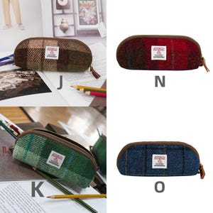 May include: A collection of eight oval-shaped pencil cases in various tweed patterns and colors, each featuring a brown zipper, a brown trim, and a white rectangular Harris Tweed label centered on the front. The options are labeled I, M, J, N, K, O, L, and P.