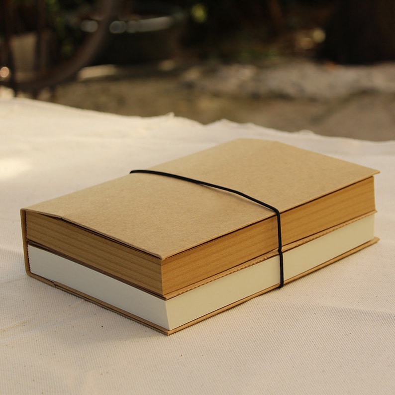 May include: A brown notebook with a brown cover and a white spine. The notebook is wrapped with a black elastic band.