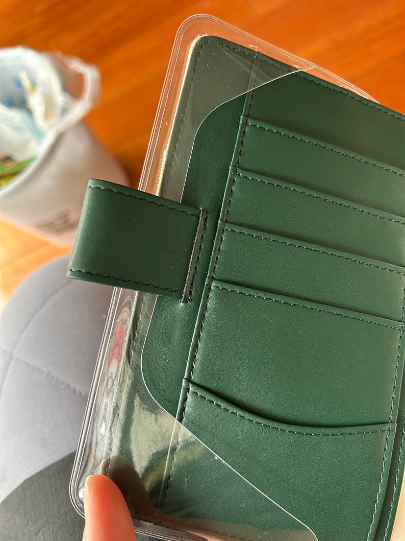 May include: A dark green leather planner with a clear plastic cover and multiple pockets. The planner has a flap closure with a black strap.