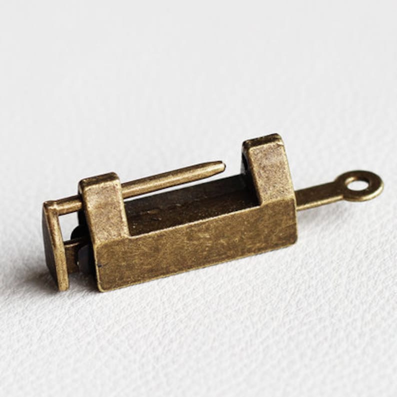 Op de afbeelding: Een klein, antiek uitziend messing hangslot met een sleutelgat en een kleine, ronde sleutelring. Het hangslot is gesloten en heeft een eenvoudig, rechthoekig ontwerp.