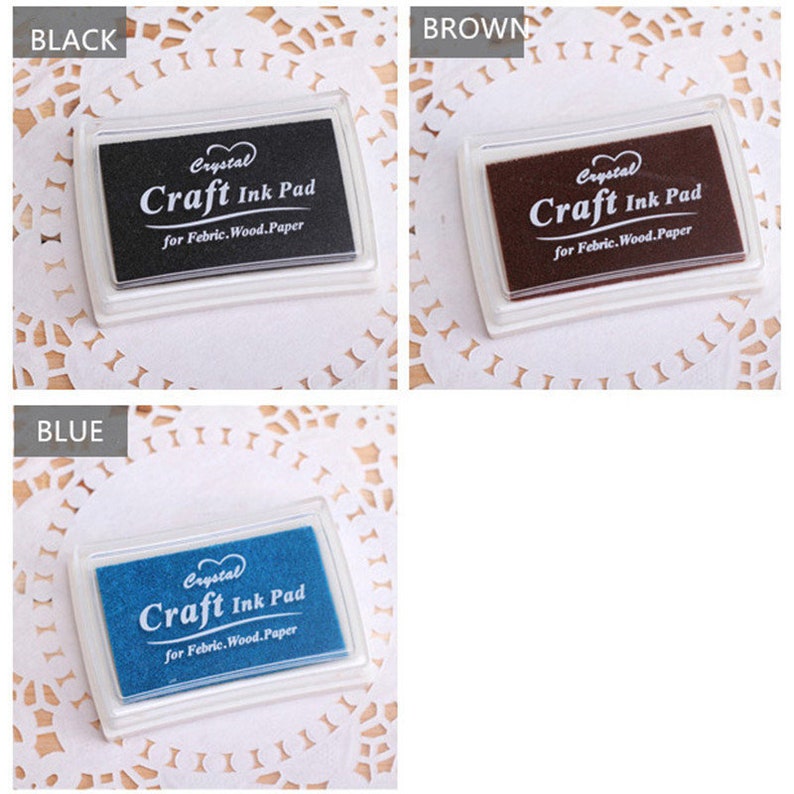 K&ouml;nnte beinhalten: Drei Stempelkissen in Schwarz, Braun und Blau. Jedes Kissen hat ein wei&szlig;es Etikett mit der Aufschrift "Crystal Craft Ink Pad for Febric.Wood.Paper".