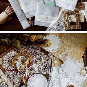 May include: A set of white lace paper die cuts featuring various designs, including butterflies, leaves, and geometric patterns. The die cuts are arranged on a wooden surface.