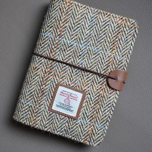 Könnte beinhalten: Ein brauner und beigefarbener Tweed-Reisepass-Etui mit einem braunen Lederriemen und einem braunen Leder-Etikett mit der Aufschrift "HAND WOVEN CLOTH Harris Tweed OUTER HEBRIDES SCOTLAND 100% PURE NEW WOOL".