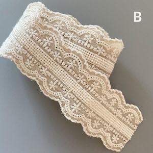 May include: A close-up of a beige crocheted lace trim with a scalloped edge. The lace has a delicate floral pattern.