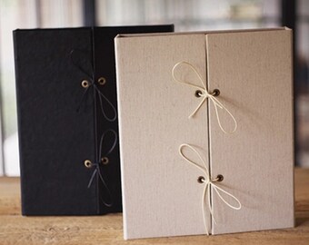 May include: Two photo albums with fabric covers. One album is black with brown string ties and the other is beige with white string ties.