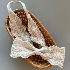 May include: A white lace headband with a bow. The headband is in a woven basket.